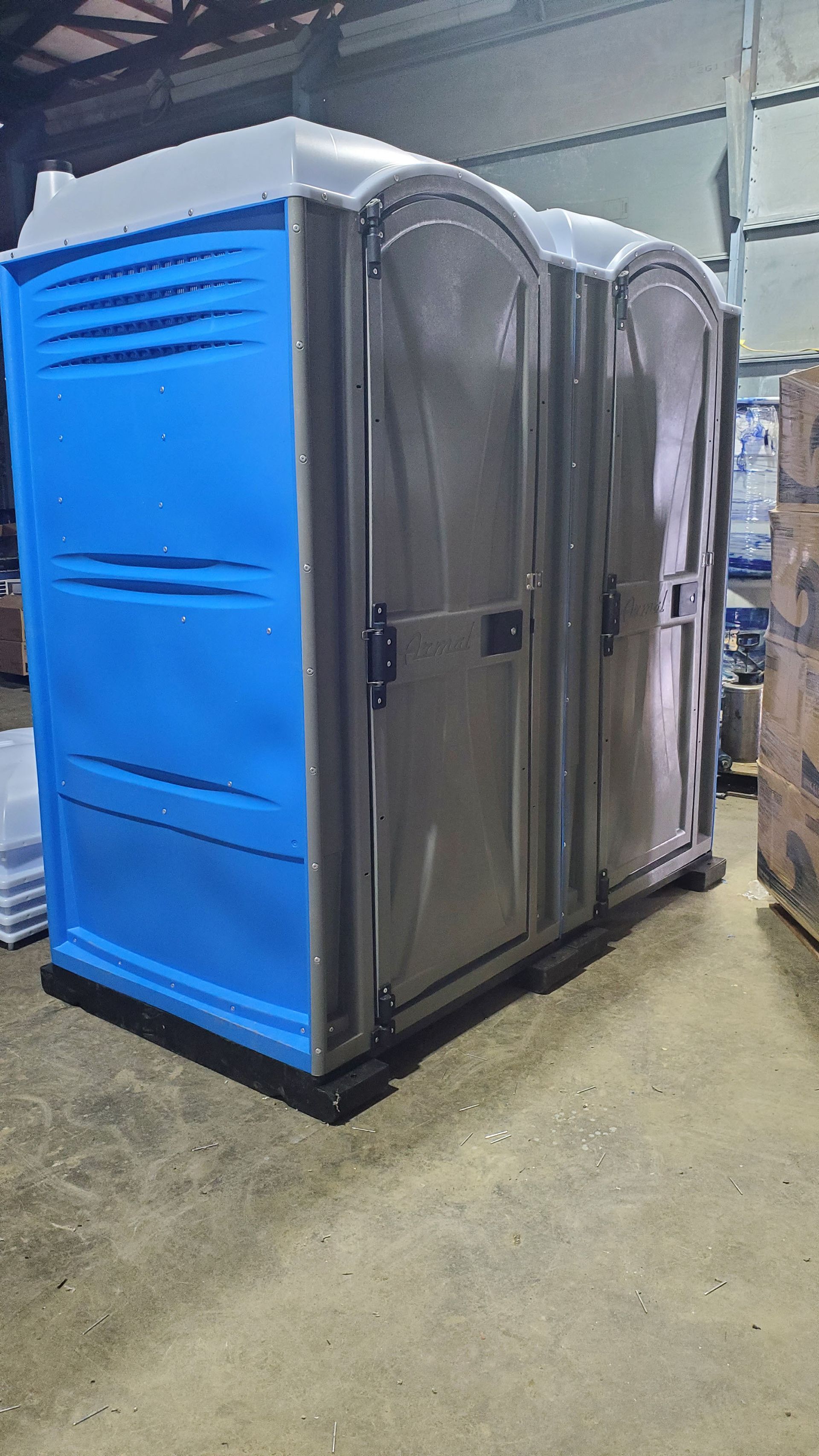 A blue and gray portable toilet is sitting in a warehouse.