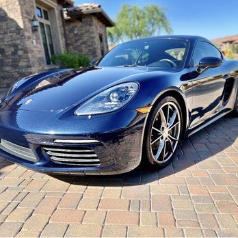 Blue Porsche coupe parked on a brick driveway in front of a house.