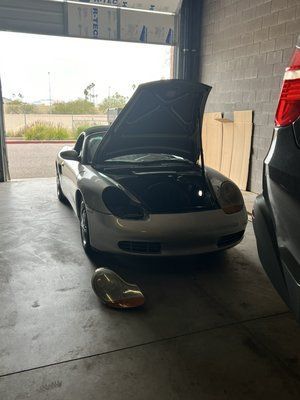 Silver Porsche with hood open in a garage, a round object on the floor.