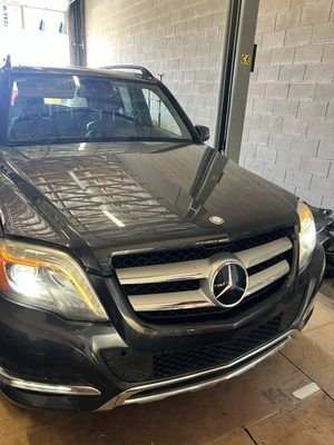 Dark gray Mercedes-Benz SUV in a garage, facing forward. Headlights on, silver grill, black hood.