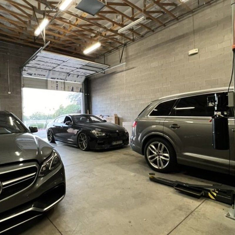 Three cars in a garage. A Mercedes, a BMW, and an Audi. The garage door is open.
