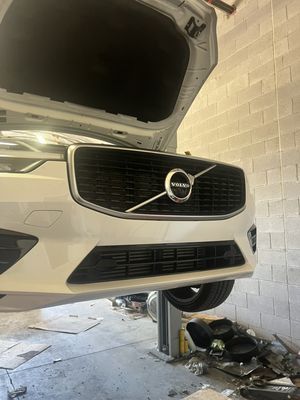 White Volvo SUV with its hood open, front end raised in a garage.