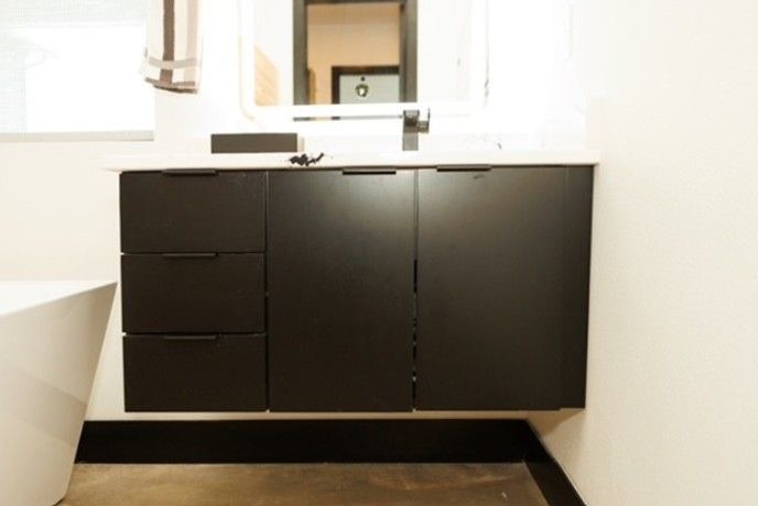 Modern bathroom vanity with black cabinets, sink, and mirror against white walls.