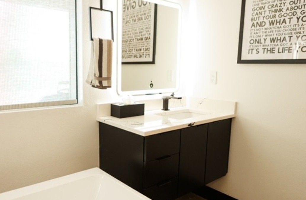 Bright bathroom with white vanity, dark cabinets, large mirror, and wall art.