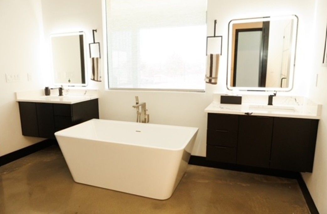 Modern bathroom with freestanding white tub, dark vanities, and large mirrors under bright windows