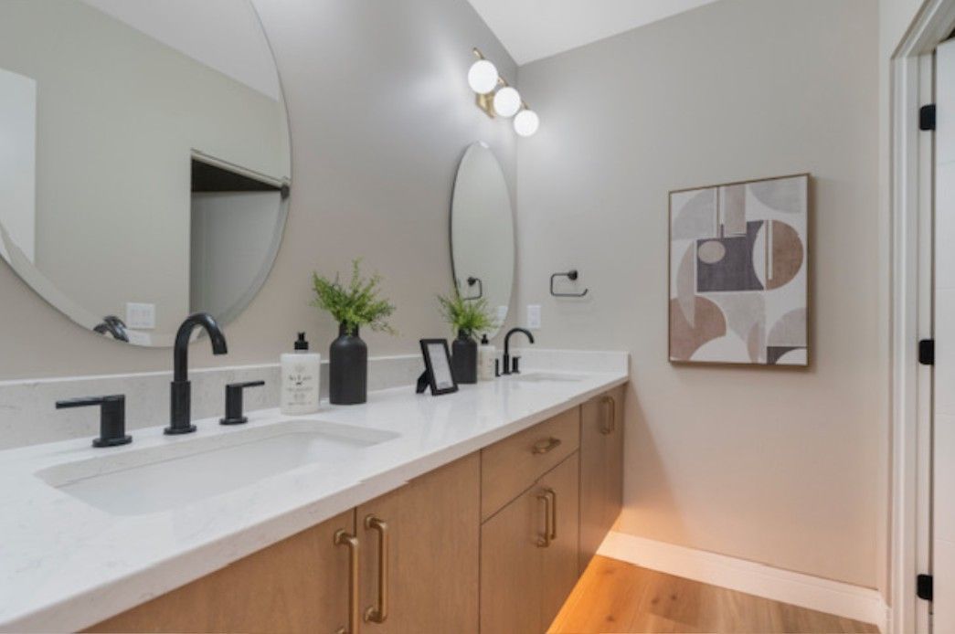Modern bathroom vanity with double mirrors, black faucets, white countertop, and warm wood cabinets