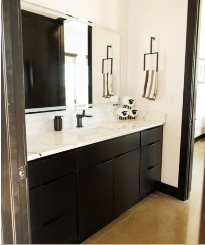 Modern bathroom vanity with black cabinets, white countertop, large mirror, and wall sconces