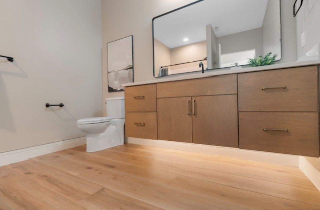 Modern bathroom with wood vanity, large mirror, white toilet, and light wood floor.