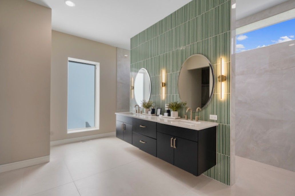 Modern bathroom with green tile wall, double vanity, round mirrors, and large window