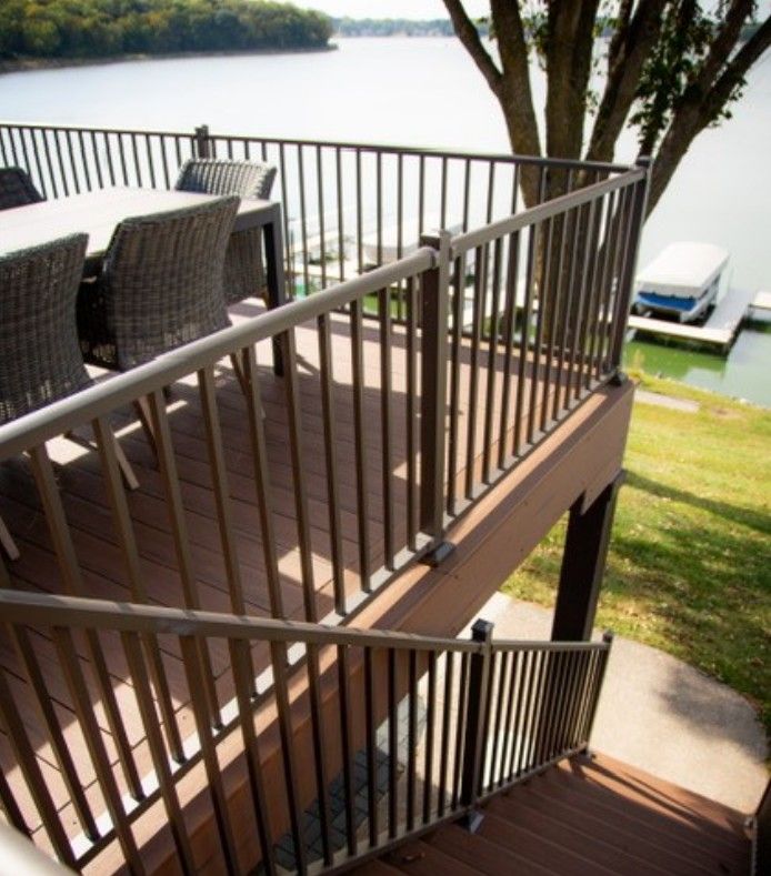 Deck with metal railings and stairs overlooking a lake, with patio furniture and a small dock below