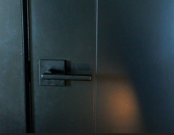 Dark metal door with a horizontal handle and a small warm light reflection