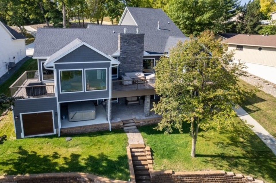 Aerial view of a gray two-story house with a front deck, lawn, and stone steps leading down to the yard