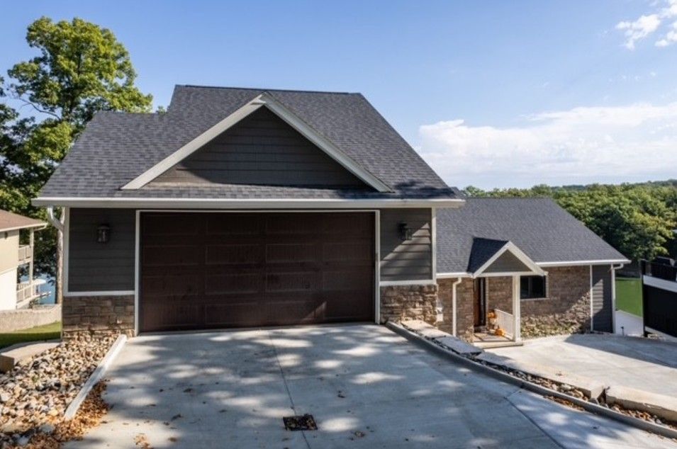 Modern two-story house with dark siding, a large garage, and a sloped driveway