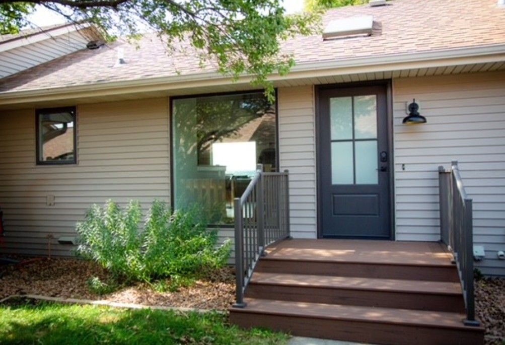 Front entrance of a house with gray siding, dark blue door, and wooden steps with railings.