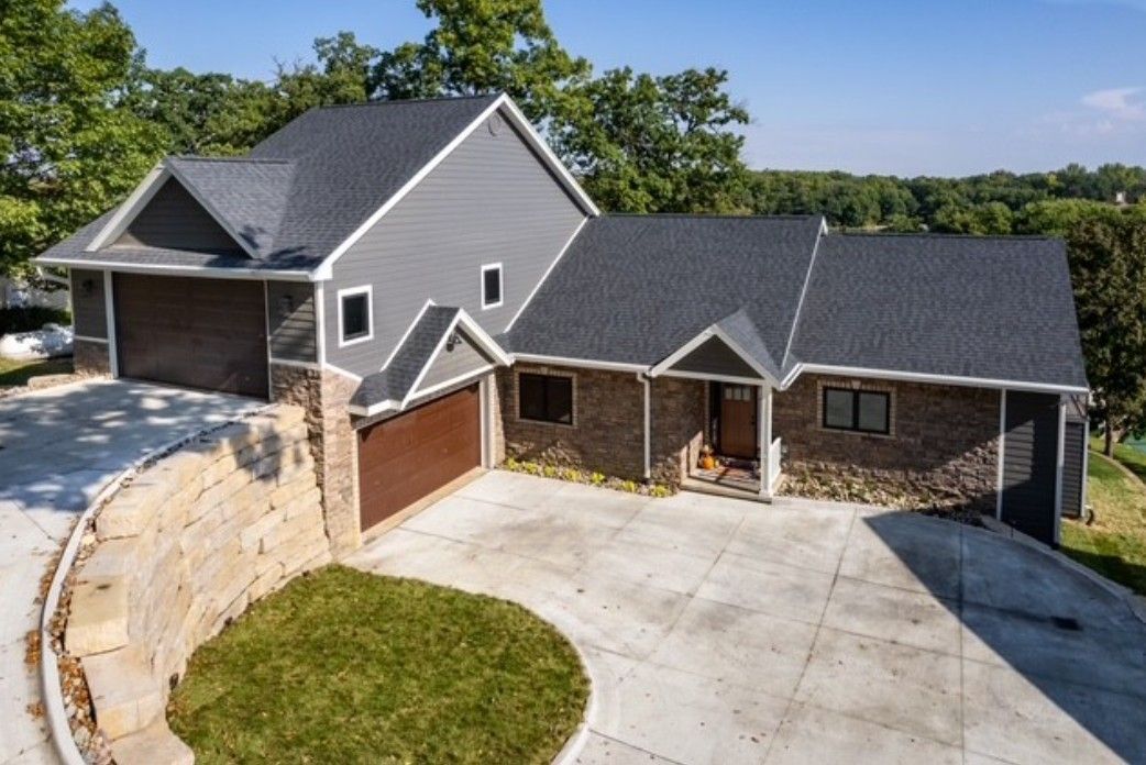 Suburban house with stone facade, gray roof, double garage, and curved concrete driveway