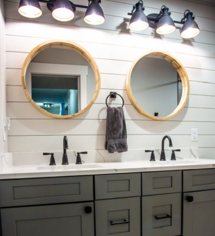 Modern bathroom vanity with two round mirrors, black faucets, and wall sconces above a double sink.