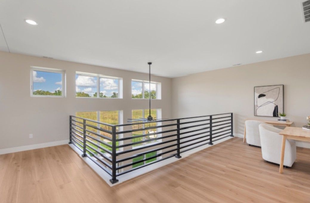 Modern upstairs landing with light wood floors, black railing, windows, and a small desk nook