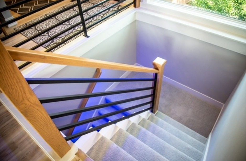Stairwell with white steps, wooden handrail, and black metal balusters viewed from above.