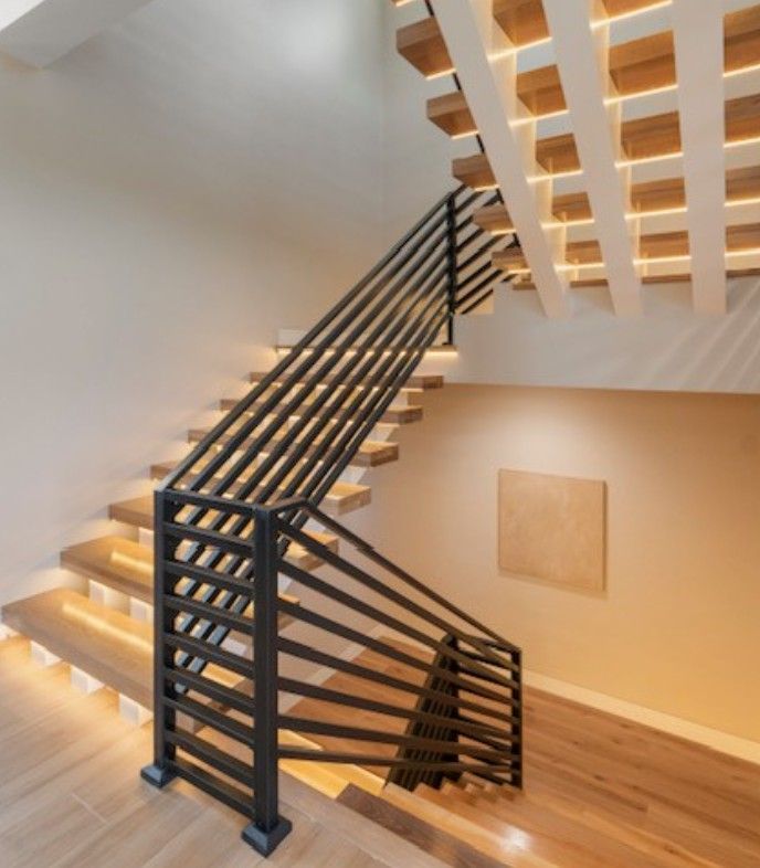 Modern indoor staircase with black railings, wooden steps, and warm lighting in a minimalist home interior