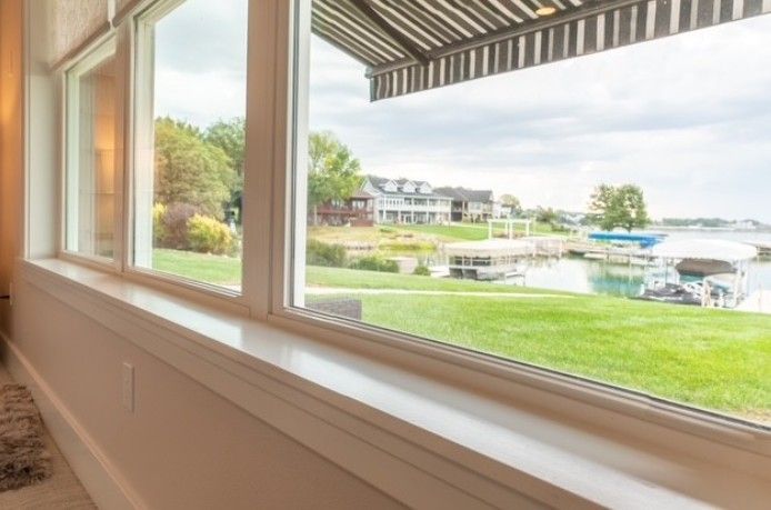 View from a window of a grassy waterfront resort with buildings, boats, and a striped awning.