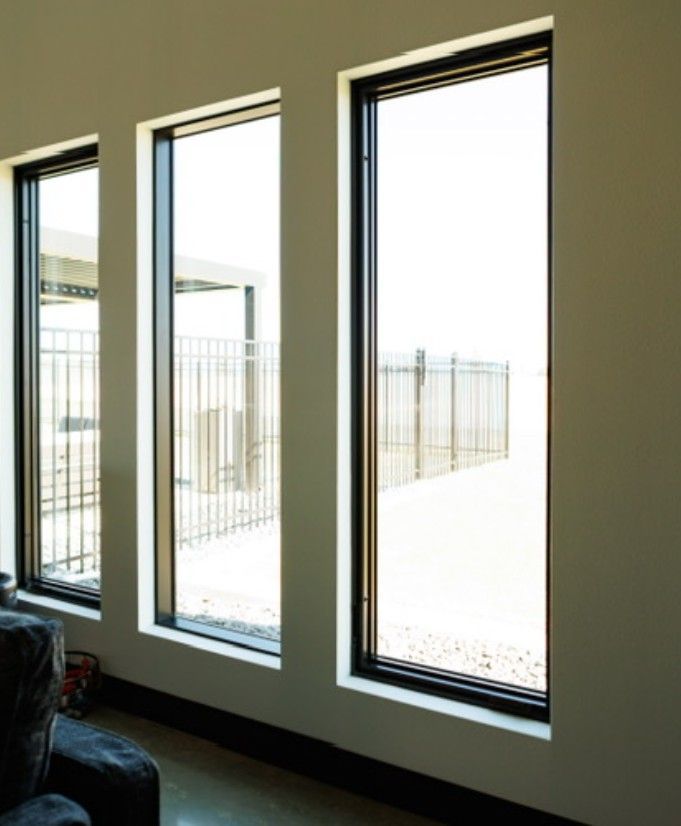 Three tall windows in a minimalist room with bright daylight and a view of a fenced balcony.