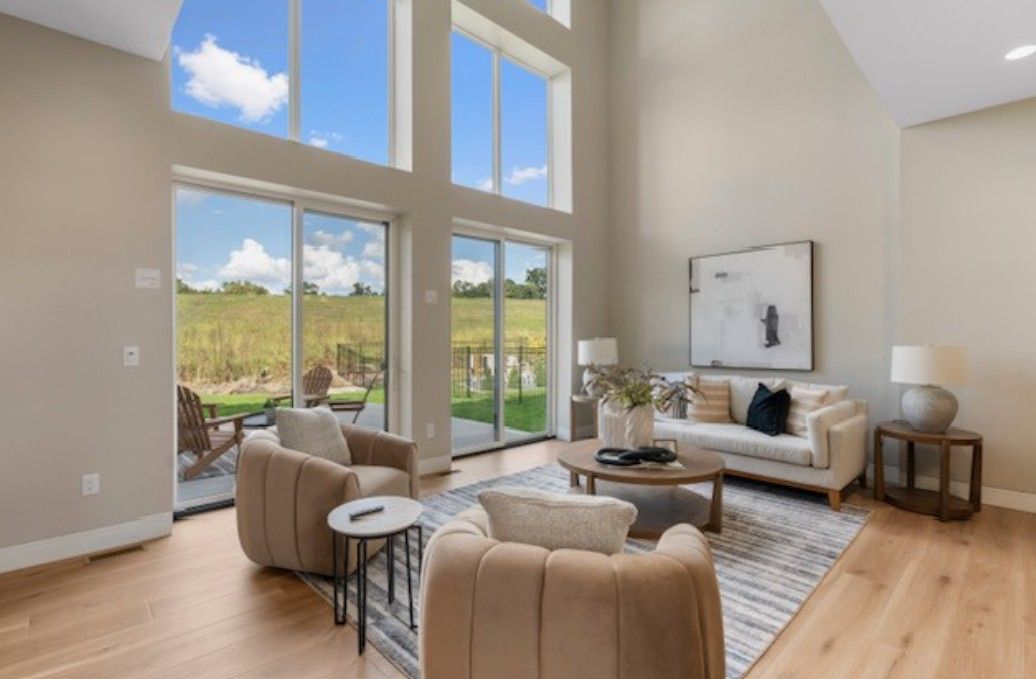 Bright modern living room with tall windows, beige furniture, rug, and view of greenery outside