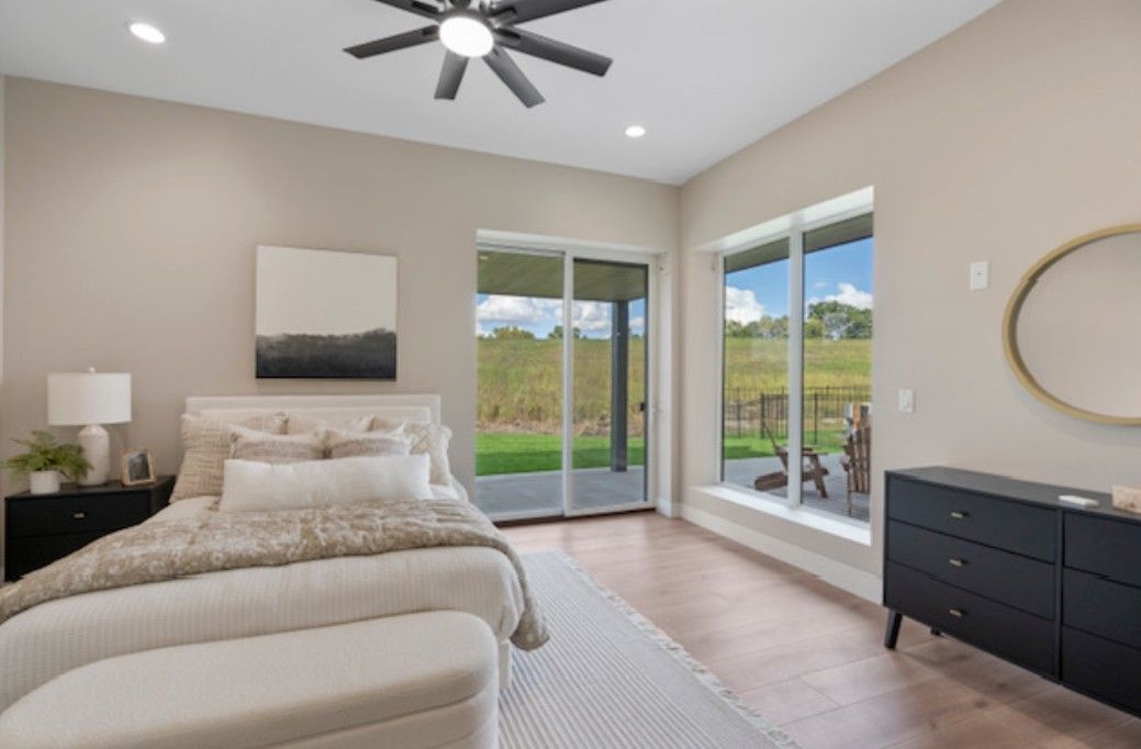 Bright bedroom with beige bed, dark dresser, ceiling fan, and sliding glass doors to a patio.