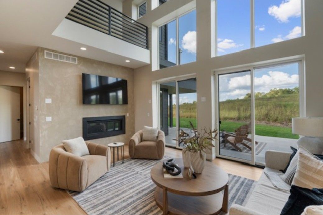 Bright modern living room with large windows, high ceiling, fireplace, and patio view