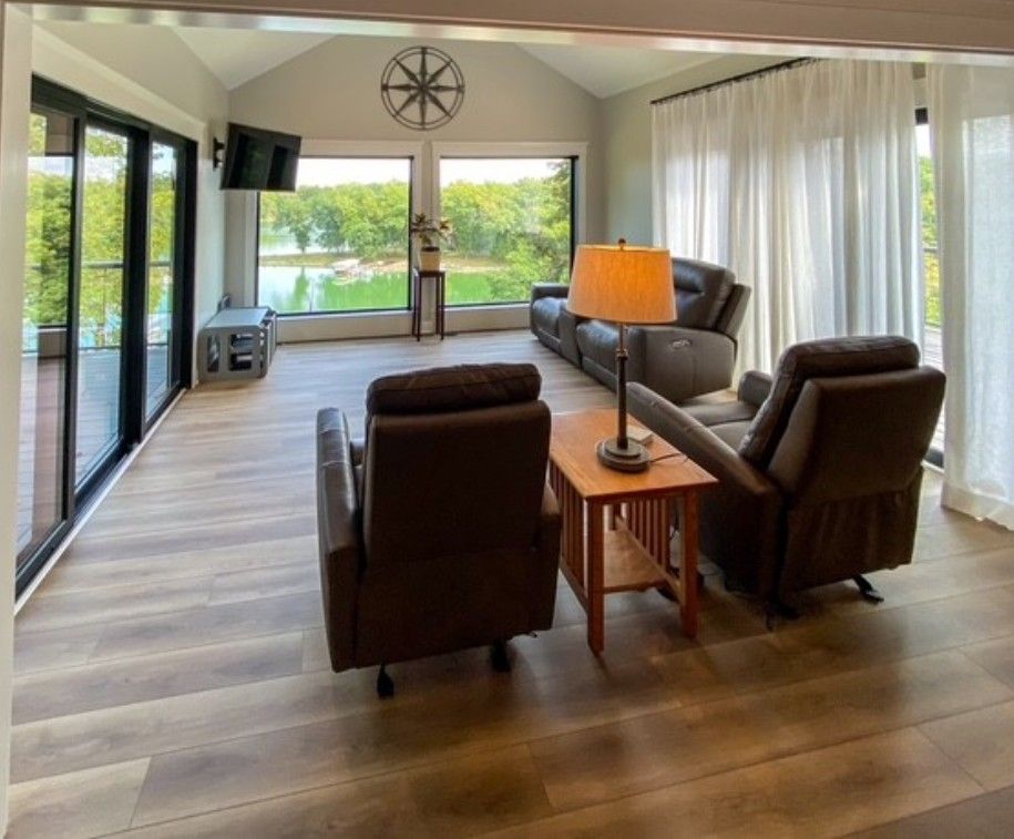 Bright living room with brown recliners, wood floor, large windows, and sliding glass doors overlooking greenery