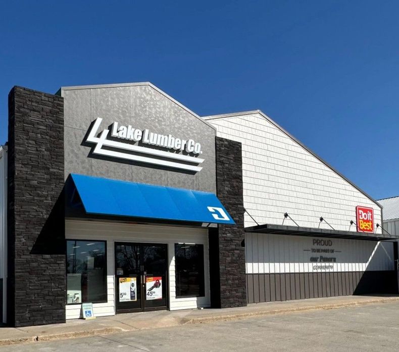 Lake Lumber Co. storefront with a blue awning, stone accents, and a Do it Best sign against a clear blue sky.