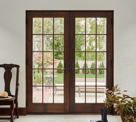 Wooden French doors with multiple panes open to a garden, framed by a white wall.