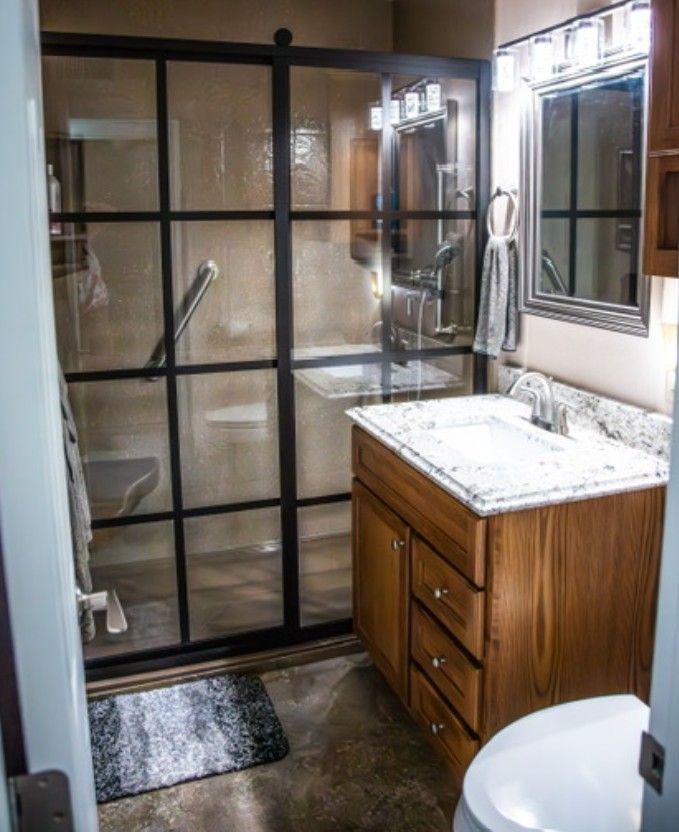 Bathroom with glass shower, wooden vanity, and white sink beside a window.