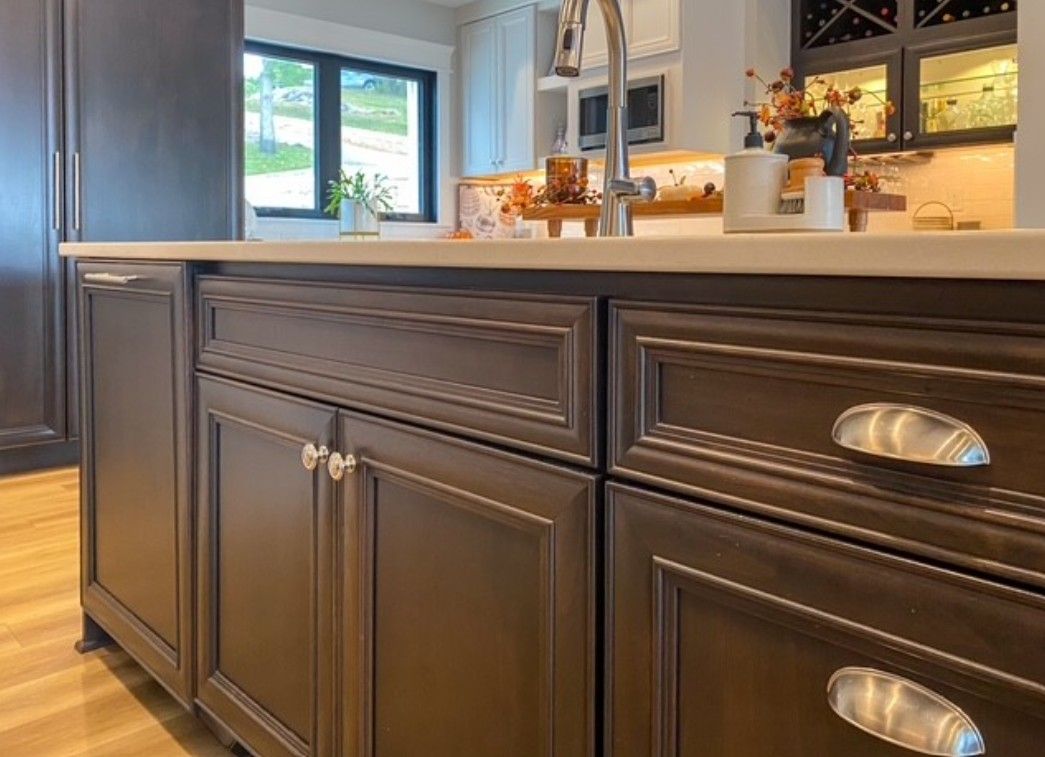 Dark wood kitchen cabinets with silver handles beneath a white countertop and a window.