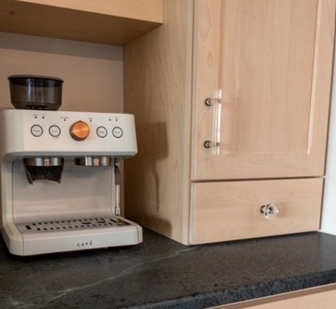 Compact espresso machine on a kitchen counter beside light wood cabinets.