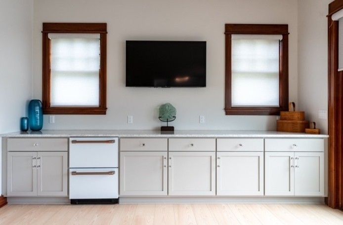 A minimalist kitchen wall with white cabinets, blue decor, two windows, and a wall-mounted TV.