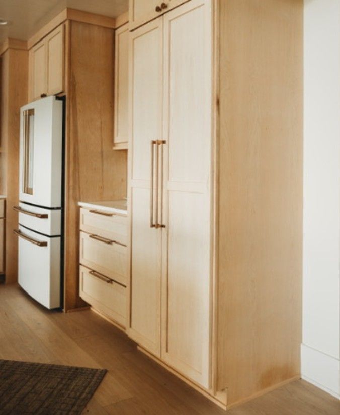 Modern kitchen with light wood cabinets, built-in refrigerator, drawers, and a tall pantry cupboard