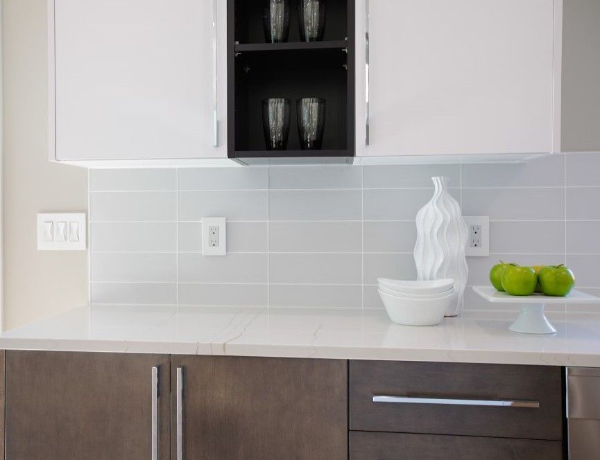 Modern kitchen with white upper cabinets, dark lower cabinets, a light gray tile backsplash, and decorative fruit display.