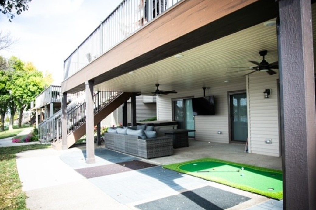 Covered outdoor patio beside a building with stairs, tables, and a green turf strip in bright daylight