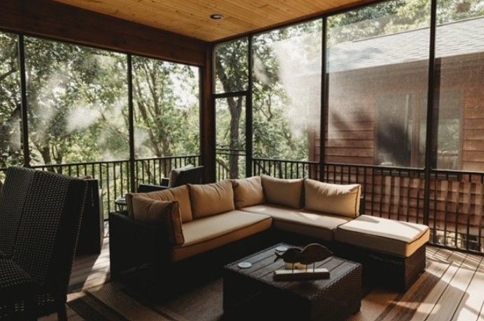 Covered patio with sectional sofa, coffee table, and wooded view through railings