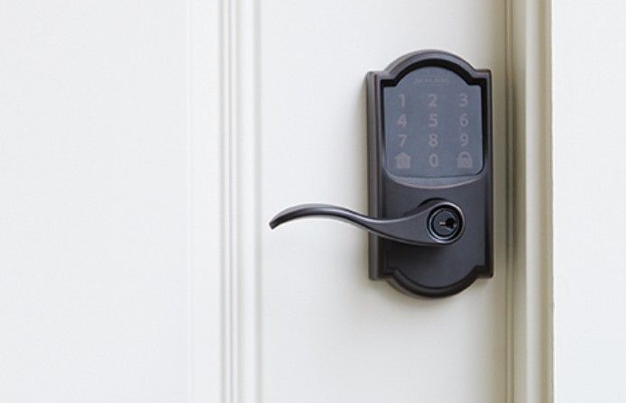A dark-colored electronic door lock with a numeric keypad and lever handle installed on a white door.
