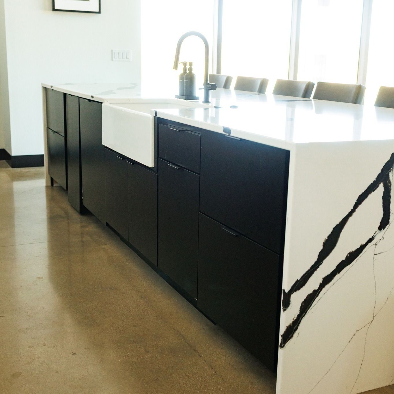 Modern kitchen island with black cabinets, white countertop, and integrated sink near large windows