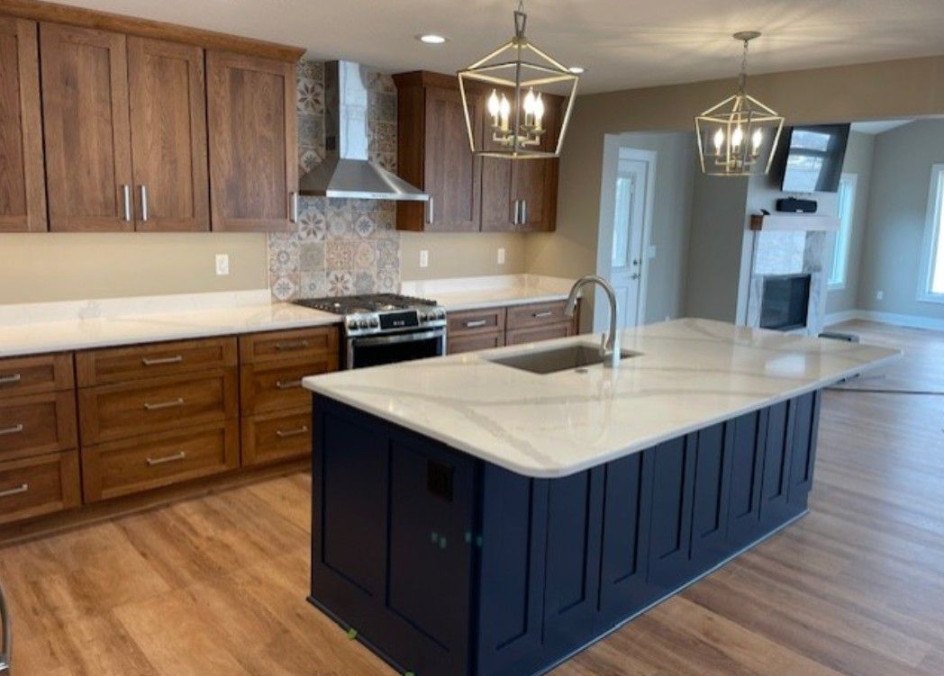 Modern kitchen with wood cabinets, white countertops, and a dark blue island with a sink