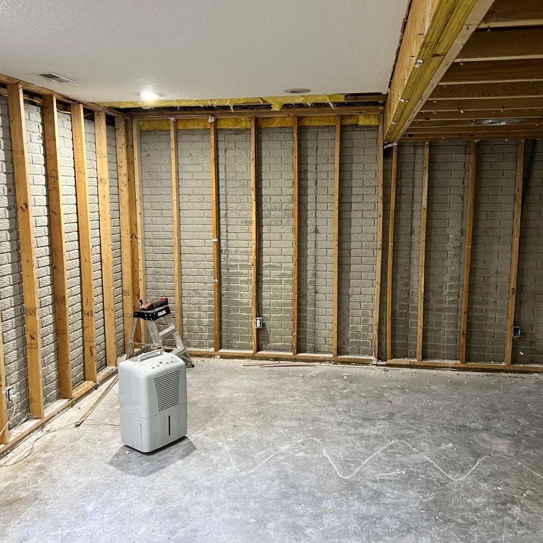 Basement interior with exposed brick walls, wooden framing, and a dehumidifier.