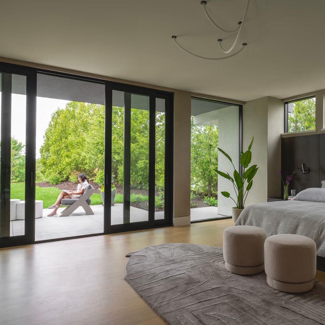 Bedroom with large sliding doors open to a backyard. A person sits outside.