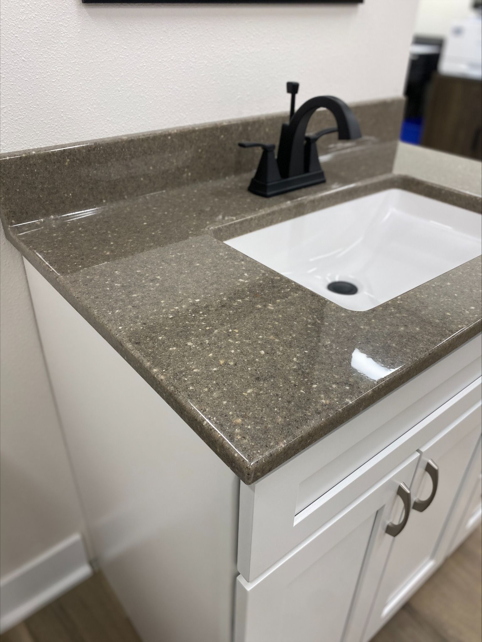 White bathroom vanity with speckled countertop and black faucet.