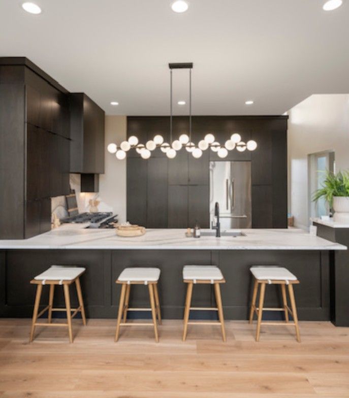 Modern kitchen with dark cabinets, large island, pendant lights, and four stools
