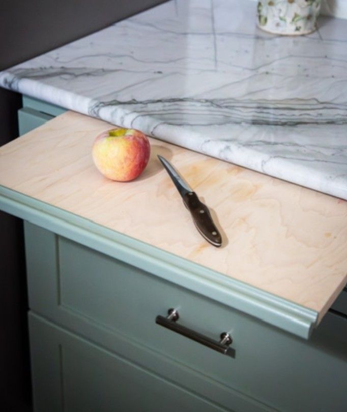 Apple and knife on a wooden cutting board beside a marble countertop