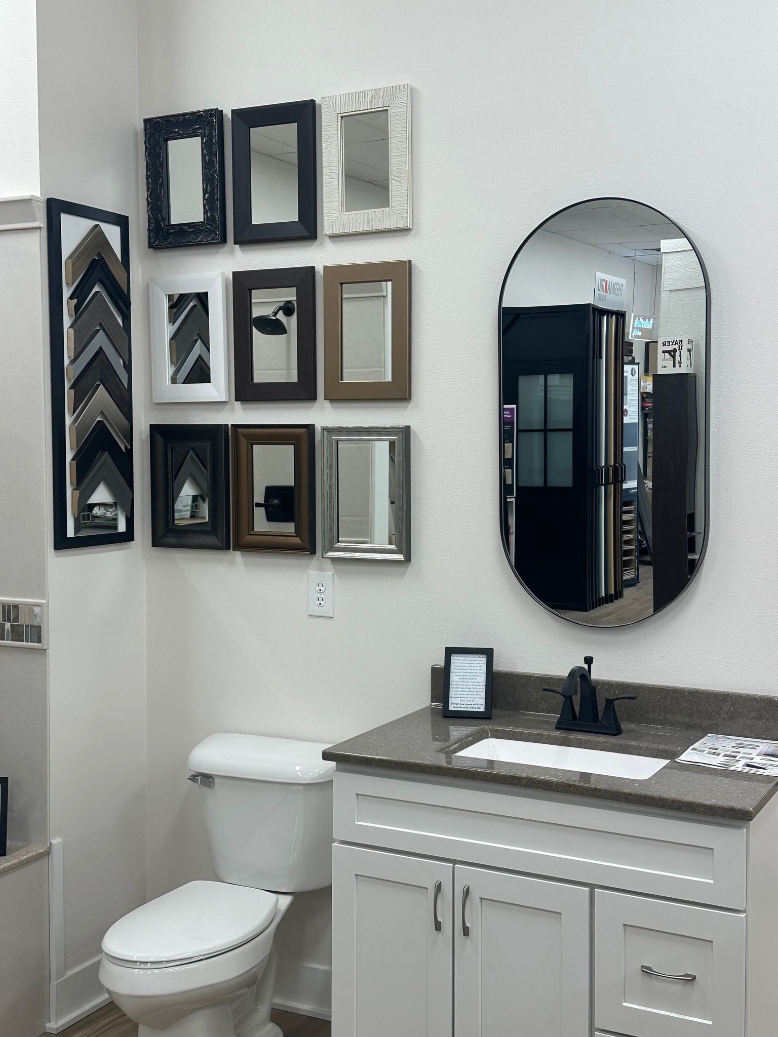Bathroom display with vanity, toilet, and framed mirrors on the wall.