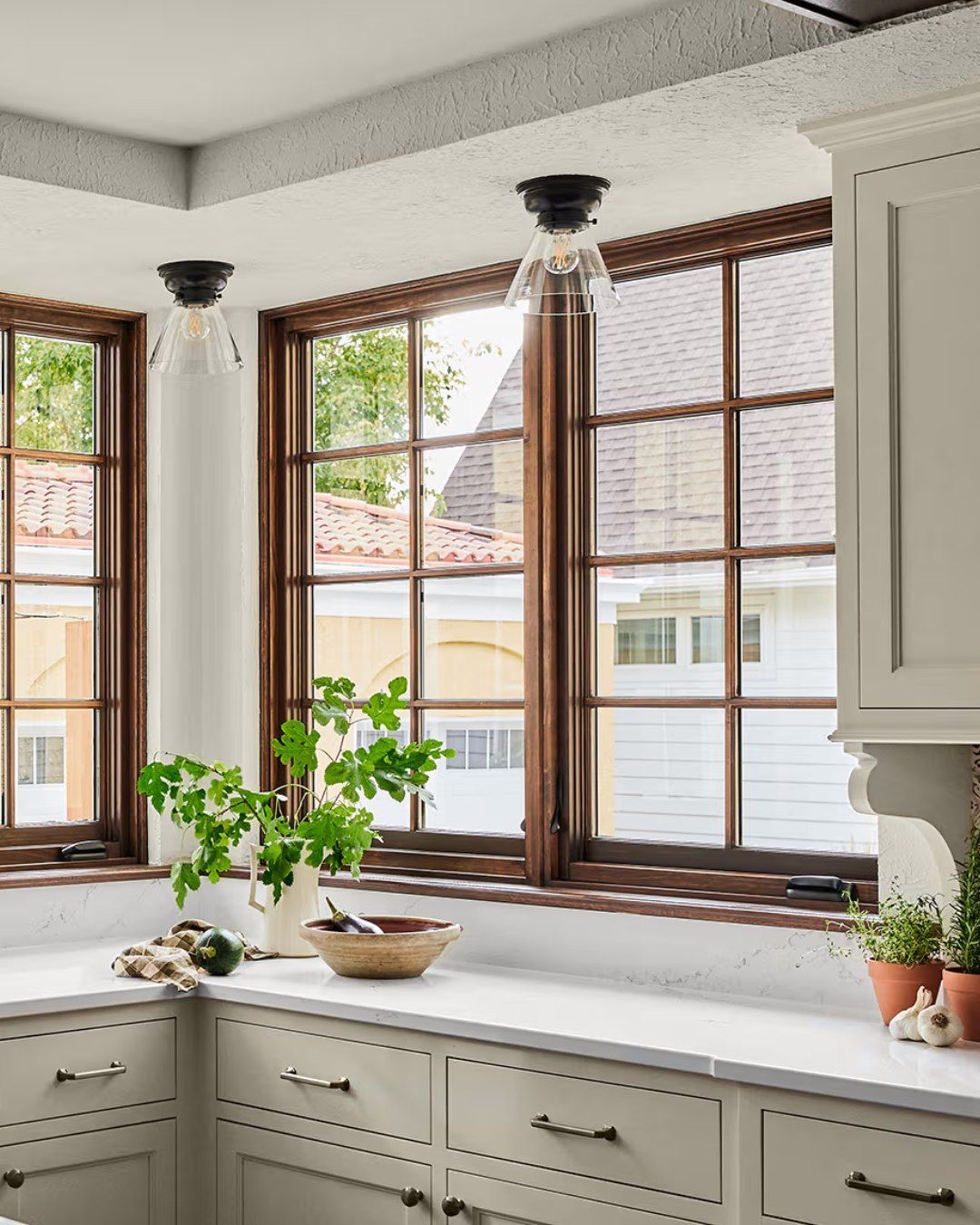 Kitchen with windows, light fixtures, cabinets, countertop, and a vase with greenery.