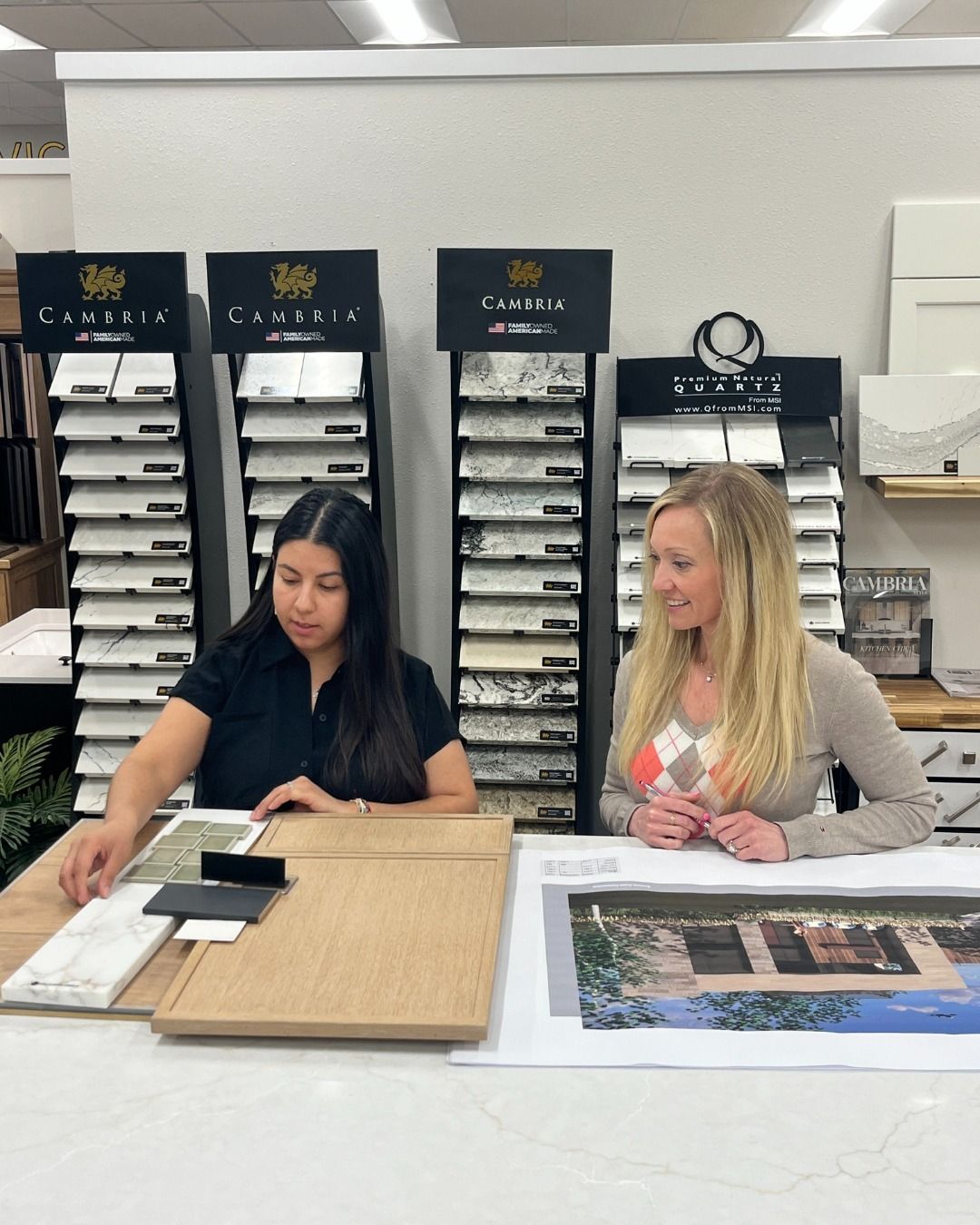 Two women selecting tile samples, reviewing a blueprint at a design center.